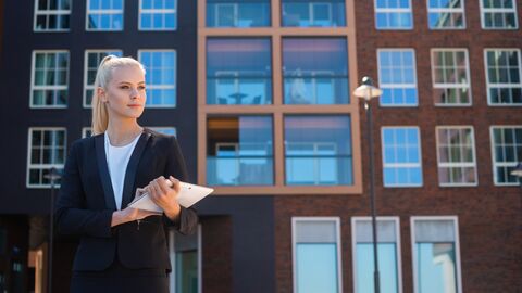 Die zum Verkauf stehenden Objekte werden vom LBIH öffentlich angeboten. Im Vordergrund ist eine Frau im schwarzen Anzug zu sehen, die gerade ein Gebäude verläßt. Sie trägt ein iPad in der Hand.